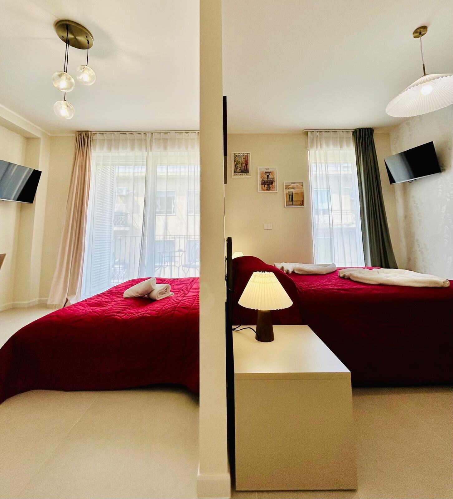 A hotel room with two beds, a flat-screen TV, a ceiling light fixture, and a window with sheer curtains.