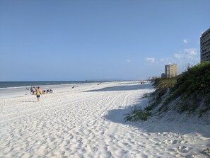 Une plage de sable avec une jetée au loin, une berge herbeuse et un bâtiment sur la droite.