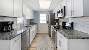 A modern kitchen with white cabinets, granite countertops, a microwave, a coffee maker, and a patterned rug.