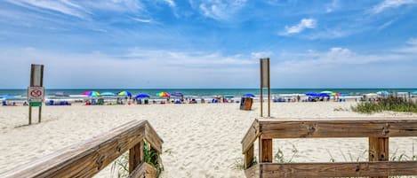 A beach with wooden boardwalks, umbrellas, and a sign prohibiting fireworks.