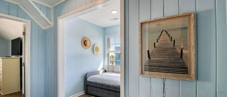 A bedroom with a bed, a dresser, a television, a framed picture, and a door leading to another room.
