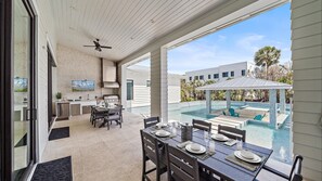 Un espace repas extérieur avec vue sur la piscine, un barbecue et un ventilateur de plafond.