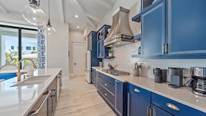 A modern kitchen with blue cabinetry, a large island, and a view of the outside.
