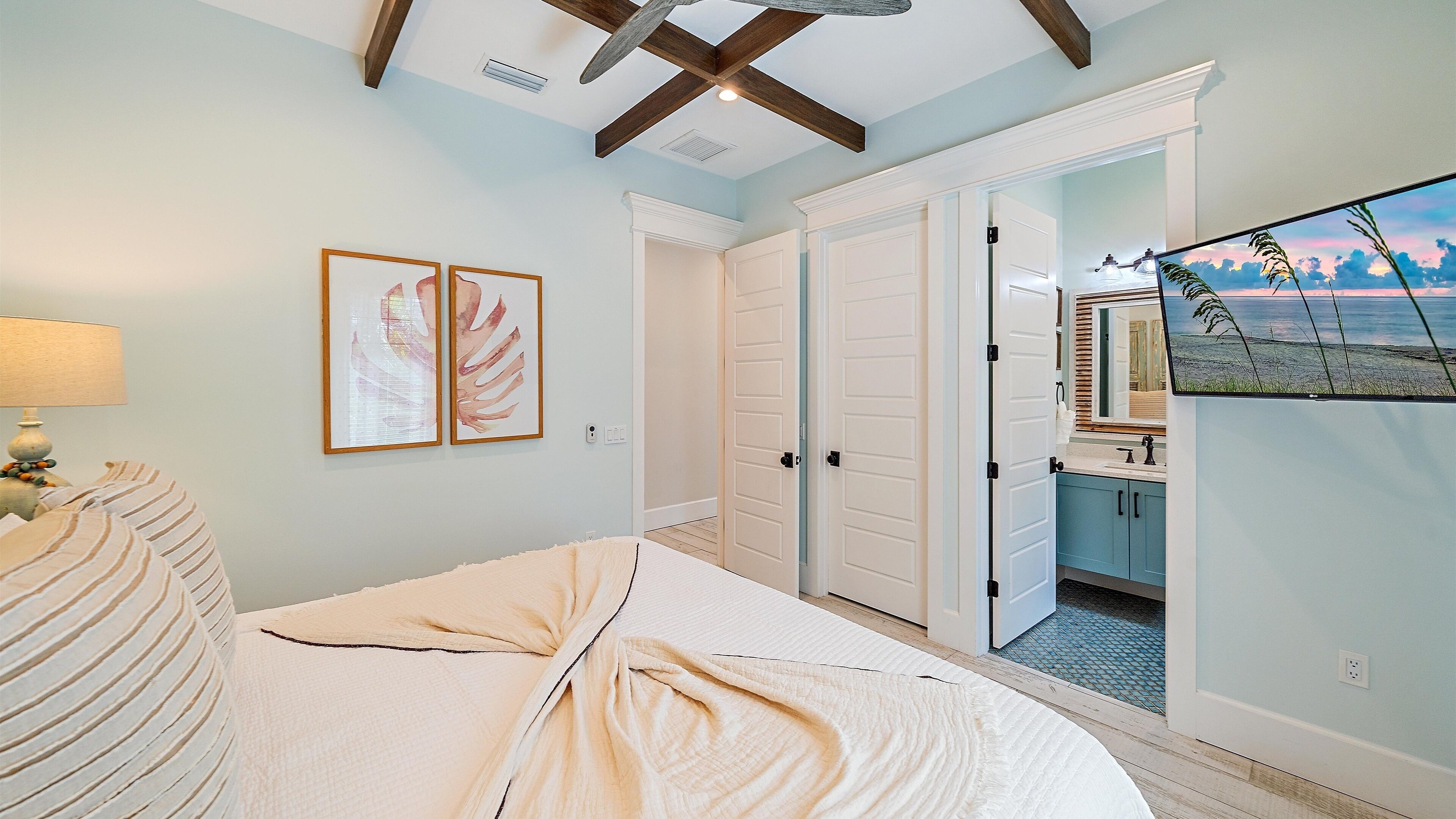 A bedroom with a bed, a nightstand, a lamp, and a wall-mounted TV displaying a beach scene.