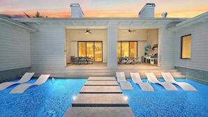 A modern outdoor pool area with lounge chairs and a patio with a dining set.