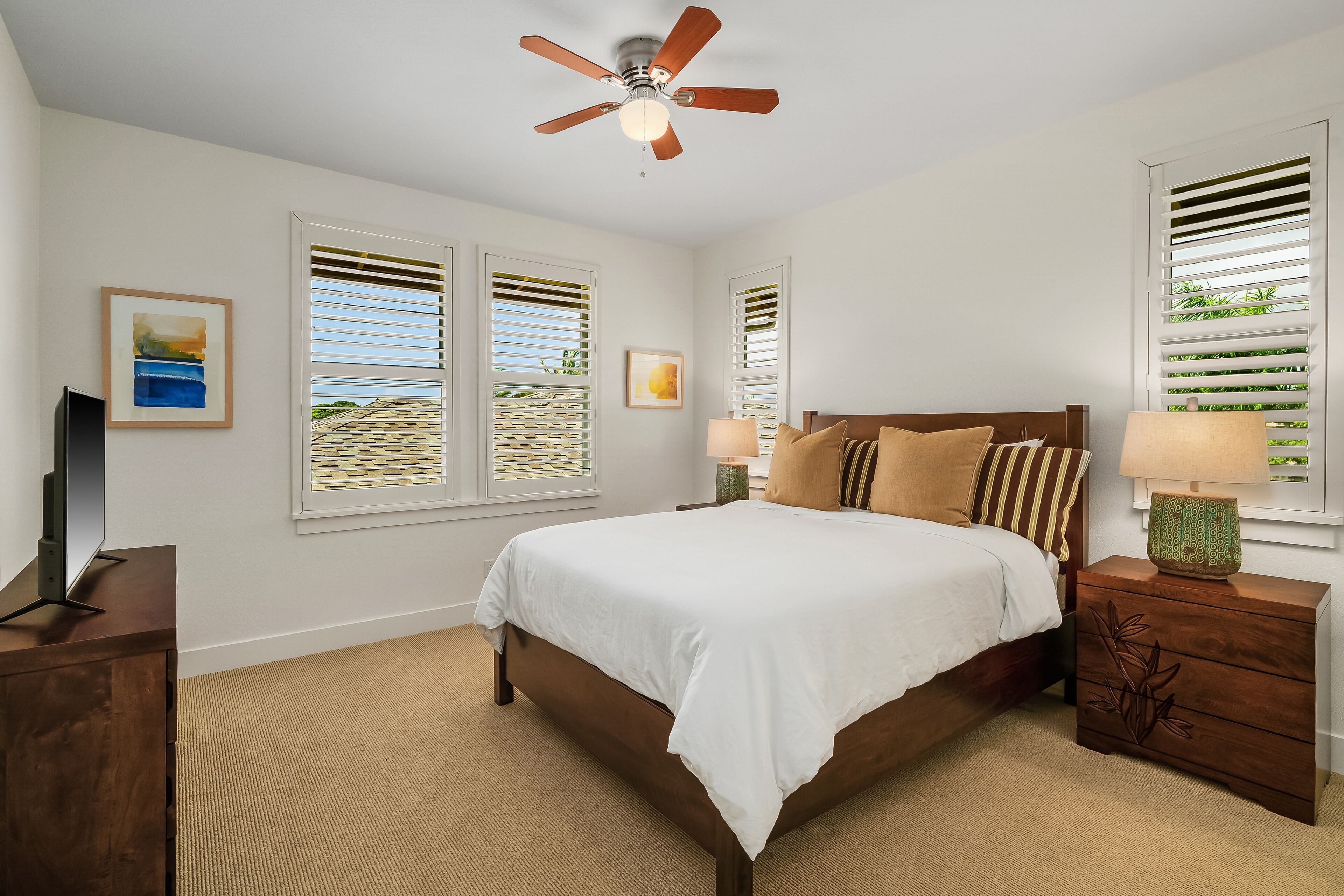 A bedroom with a bed, nightstands, a ceiling fan, and windows with blinds.