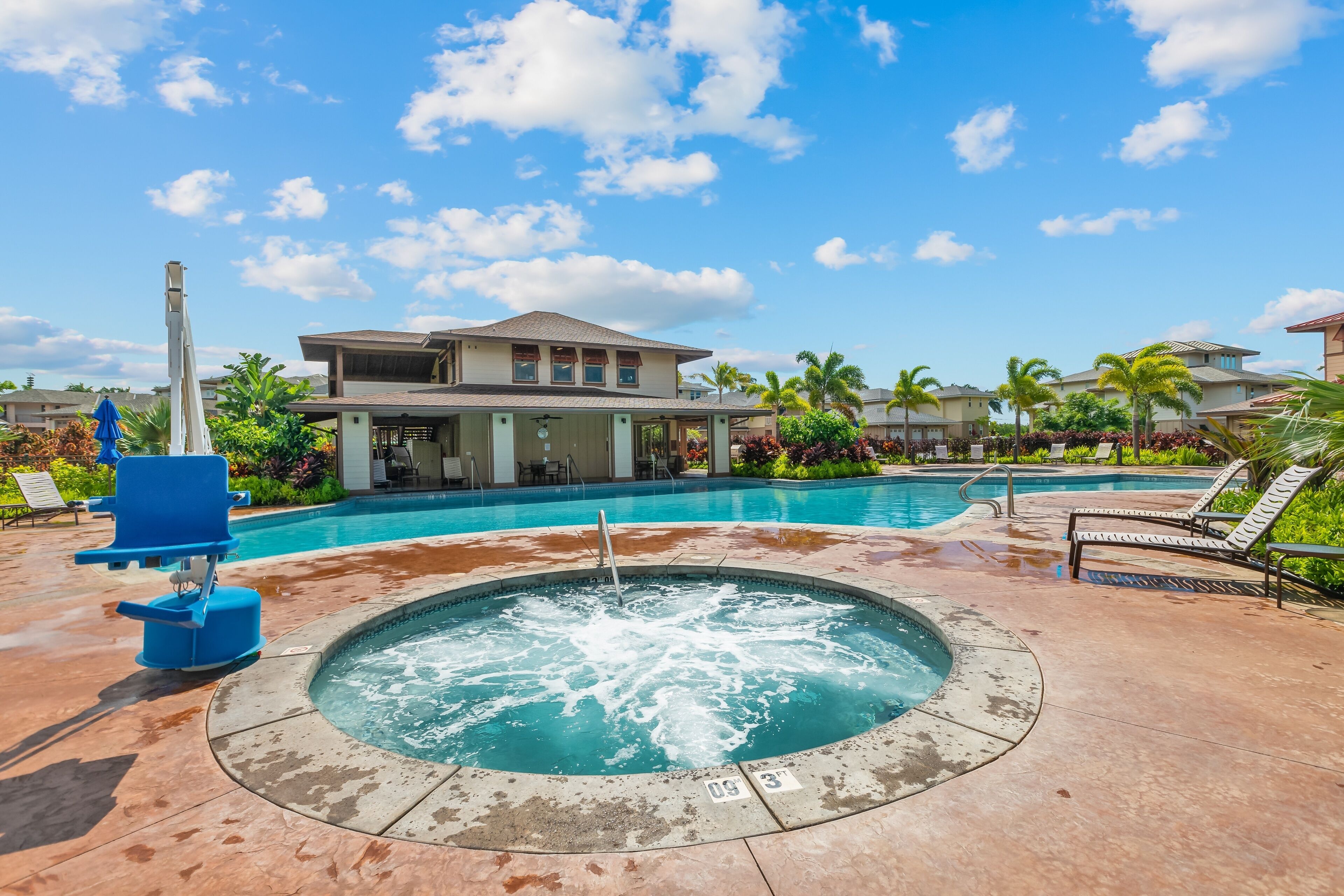 A pool area with a hot tub, lounge chairs, and a house in the background.