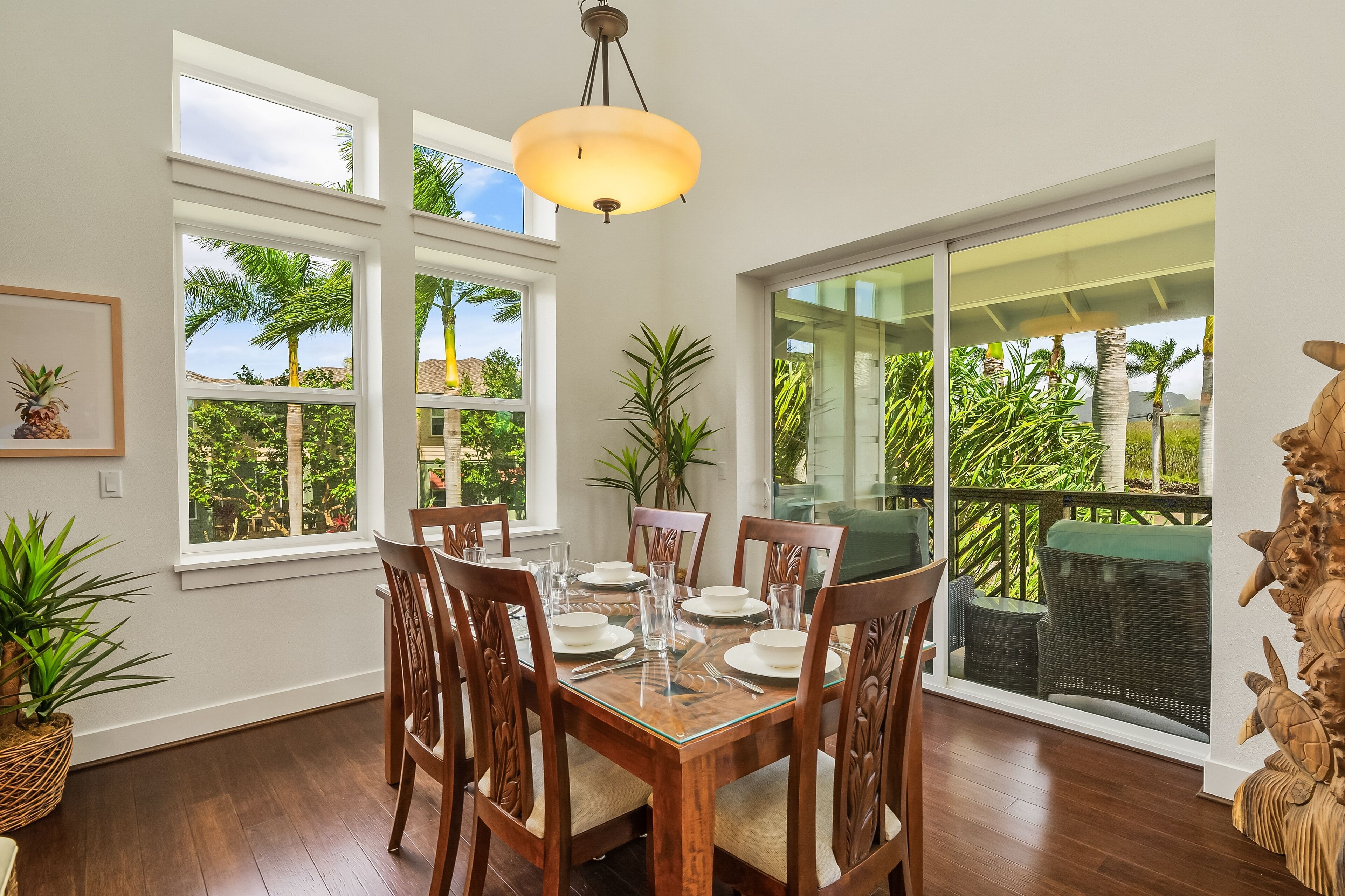 Un comedor con mesa de madera dispuesta para cuatro personas, ventanas amplias y vistas a vegetación tropical.