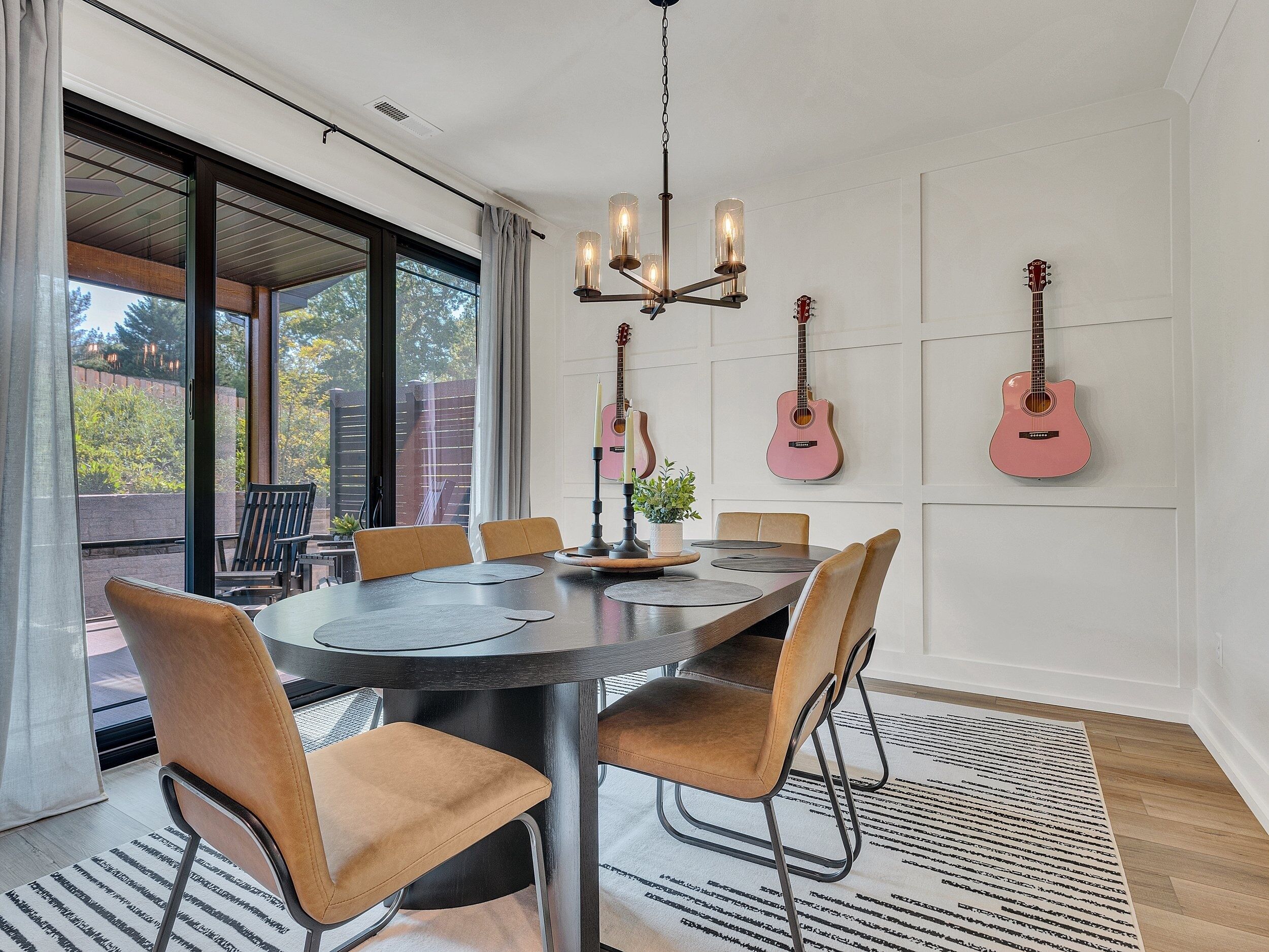 Un coin repas avec une table ronde, des chaises, un lustre et des guitares accrochées au mur.