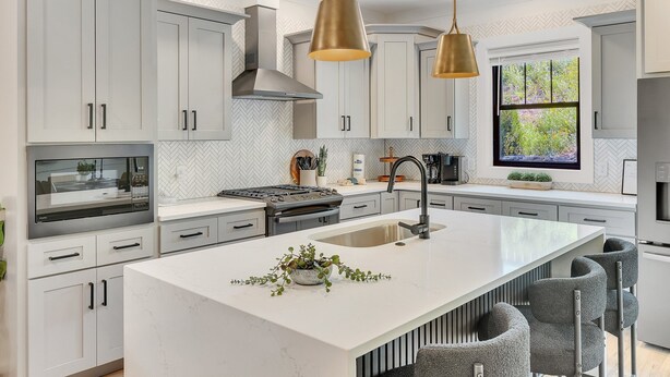 A modern kitchen with white cabinetry, a central island, stainless steel appliances, and pendant lighting.