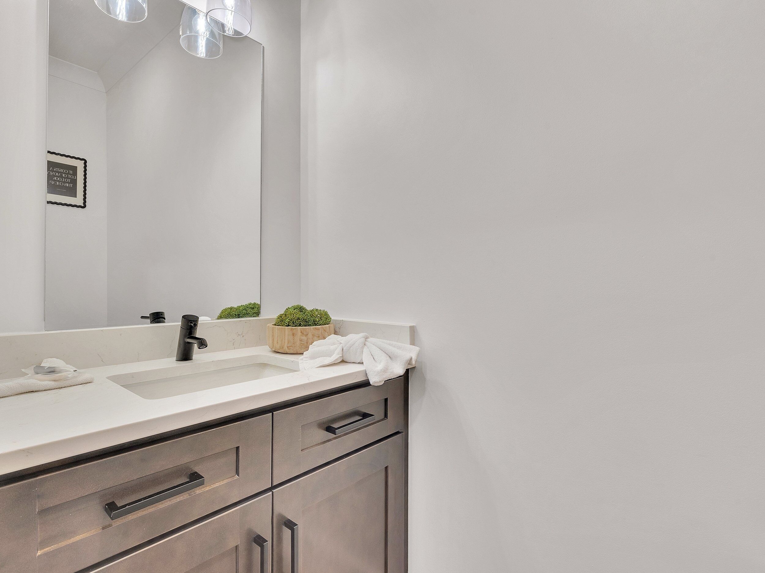 A modern bathroom with a white sink, a mirror, a small potted plant, and a towel.