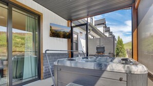 A modern outdoor hot tub with a view of a mountain landscape, a grill, and a sliding glass door.