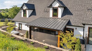 A modern two-story house with a sloped roof, a covered patio, and a landscaped garden.