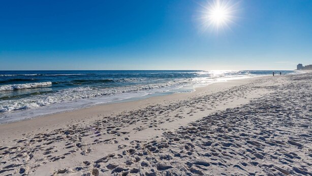 A beach with footprints, waves, and a clear sky.