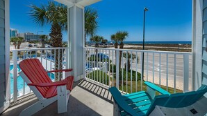 A balcony with red and blue Adirondack chairs, a pool, and a view of the beach and ocean.