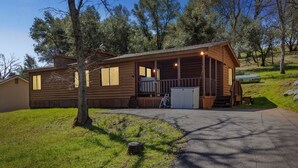 A wooden cabin with a porch, a garage, and a small deck. - Lincoln Lodge 2 Bedroom Cabin by Yosemite Region Resorts (Groveland)