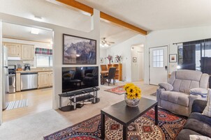 A modern living room with a TV, comfortable seating, and a dining area in the background.