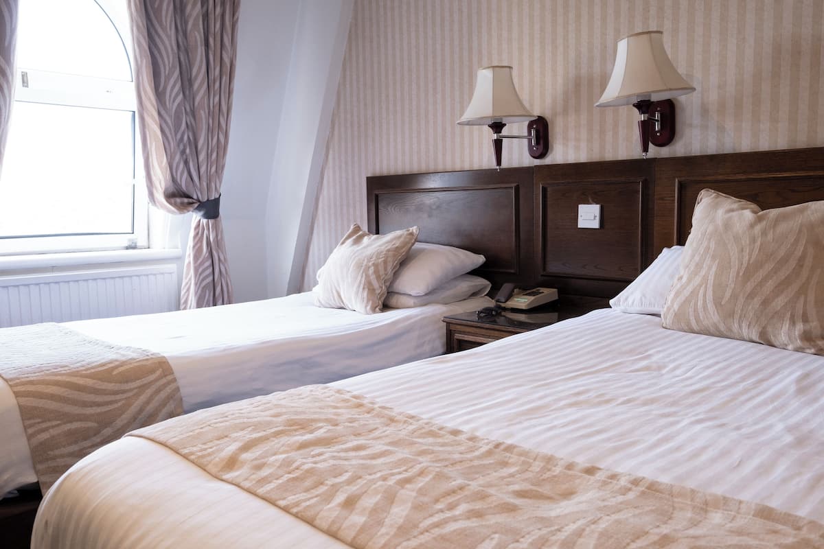 A hotel room with two beds, a nightstand with a lamp, and a window with curtains.