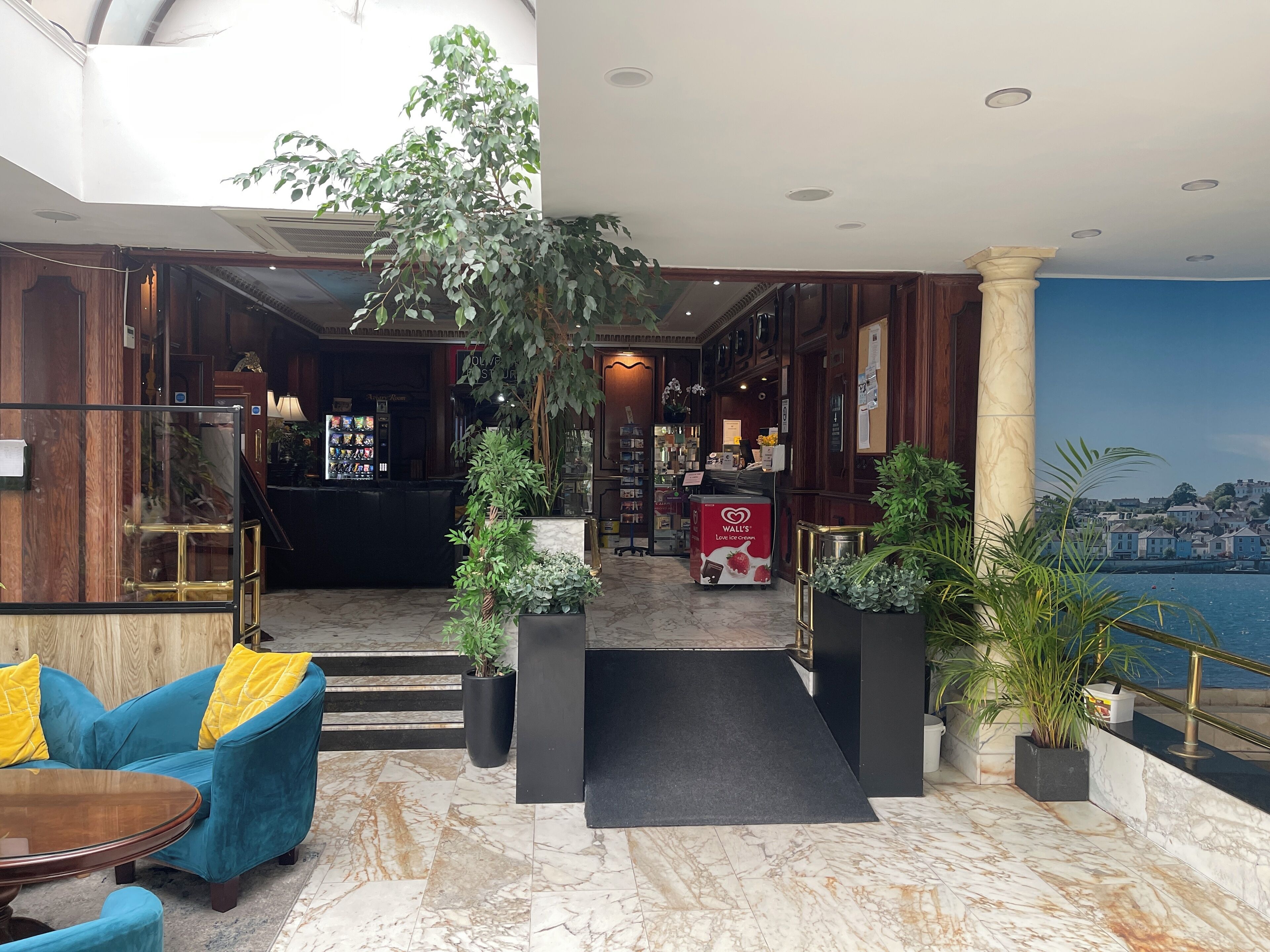 A hotel lobby with a marble floor, a reception desk, a blue sofa, and a large potted plant.