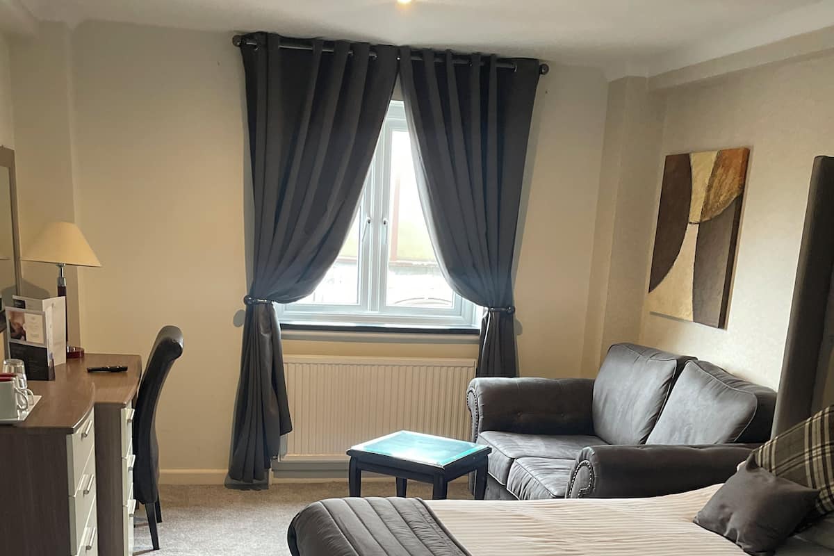 A hotel room with a large bed, a smaller bed, a desk, a chair, and a window with curtains.