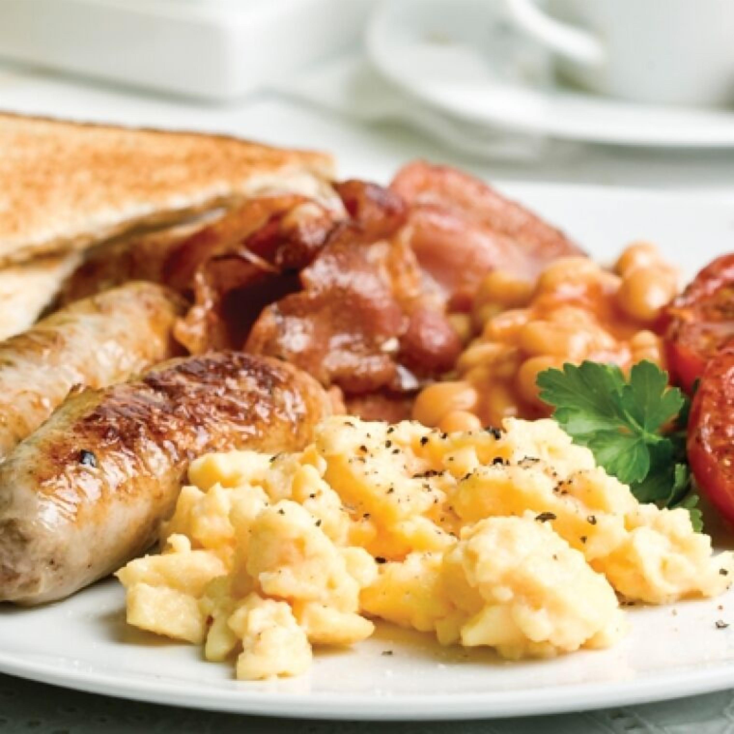 Ein Teller mit Rührei, Würstchen, Speck, Toast und Tomaten.