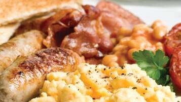 A plate with scrambled eggs, sausages, bacon, toast, and tomatoes.