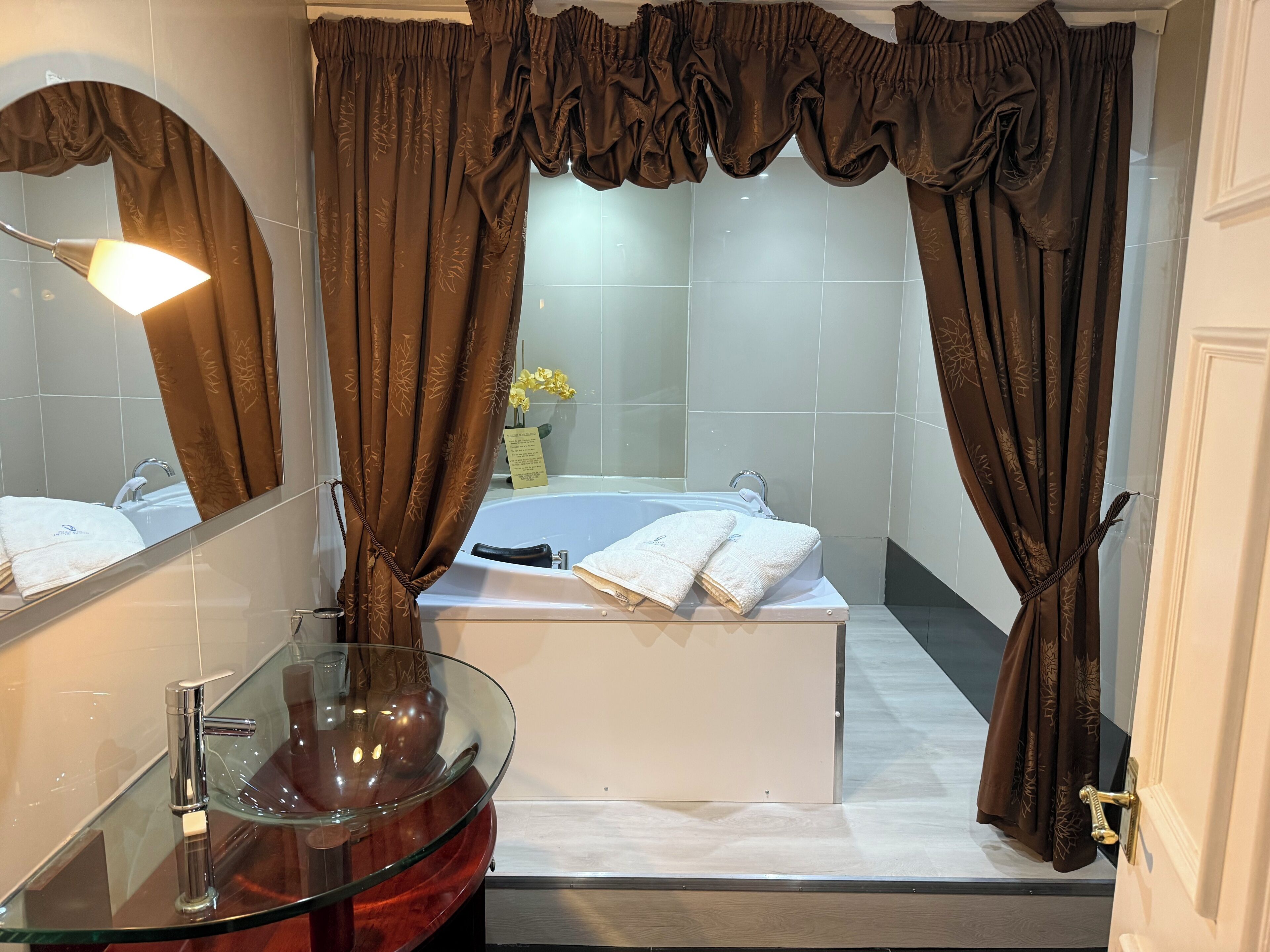 A bathroom with a glass sink, a bathtub, and brown curtains.