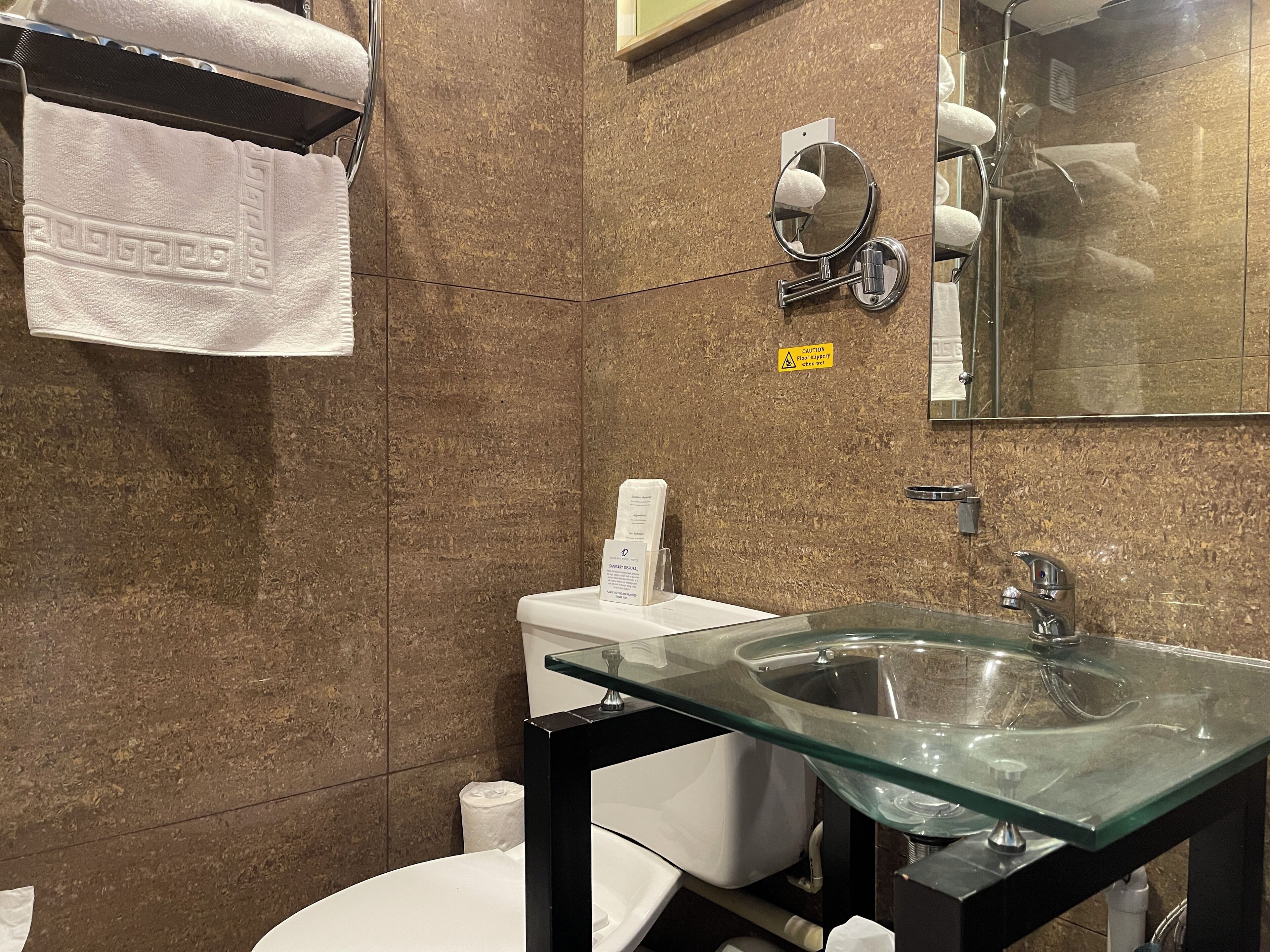 A modern bathroom with a glass sink, a toilet, and a towel rack.