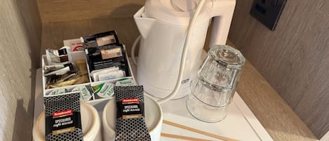 A breakfast setup with coffee mugs, tea packets, a glass of water, and a coffee maker on a countertop.