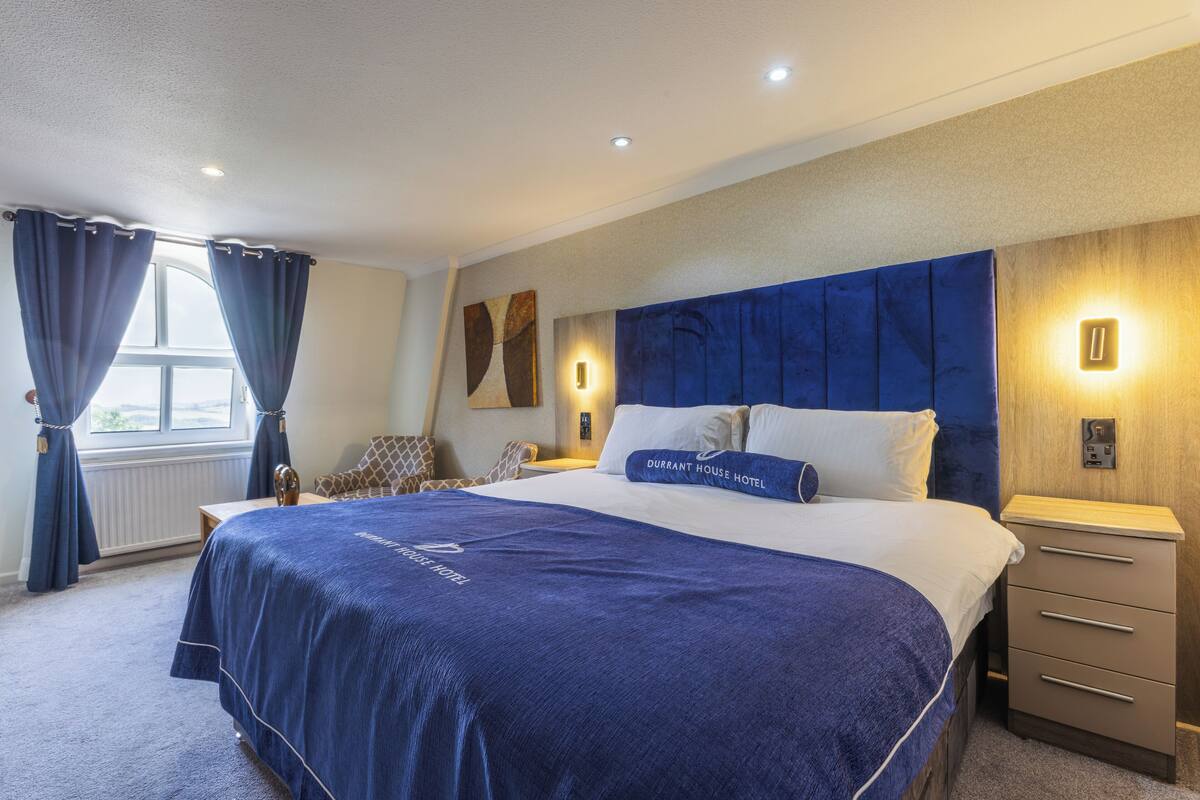 A hotel room with a large bed, a nightstand, a chair, and a window with curtains.