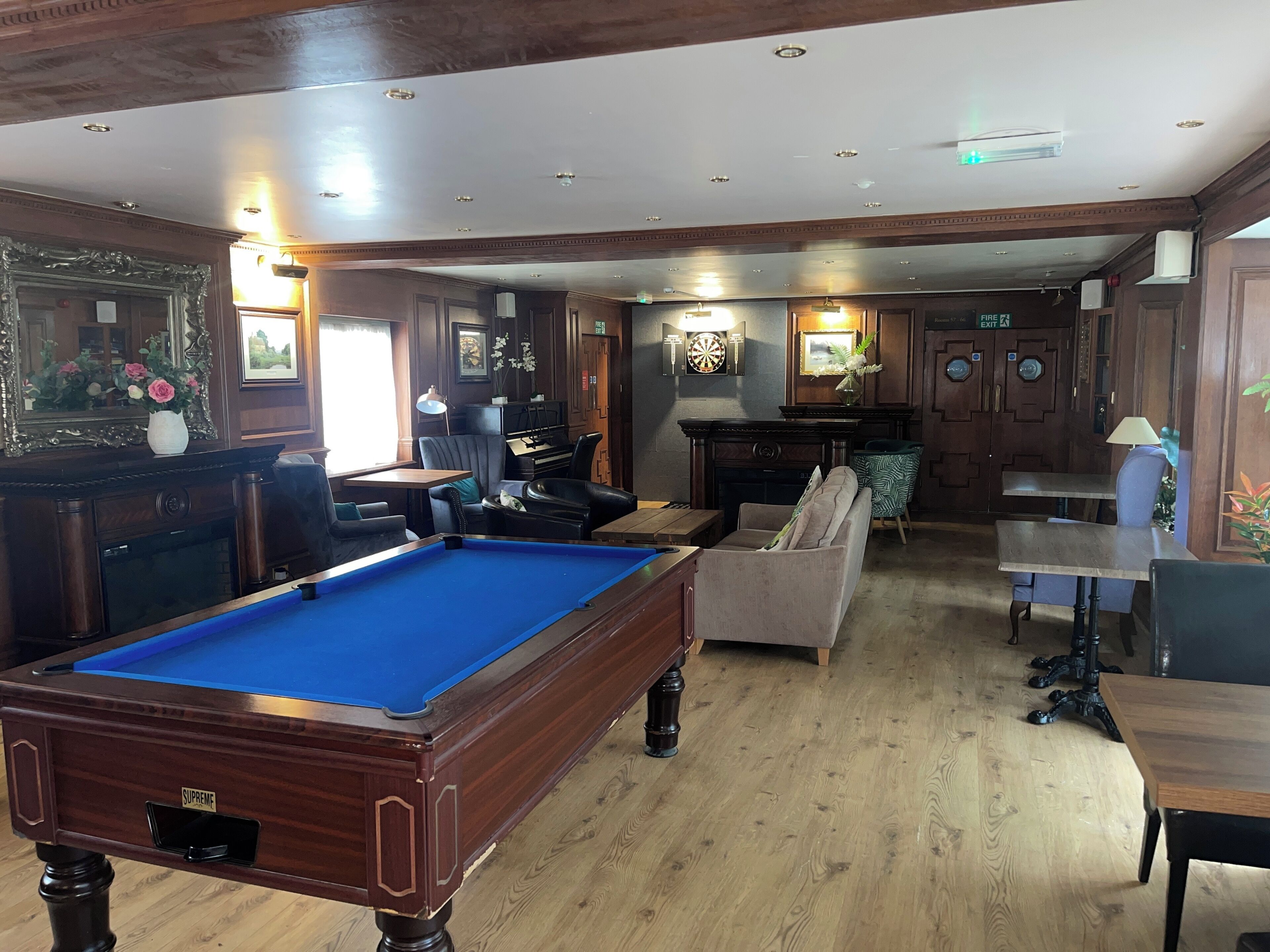 A billiards room with a pool table, seating, and a dartboard.