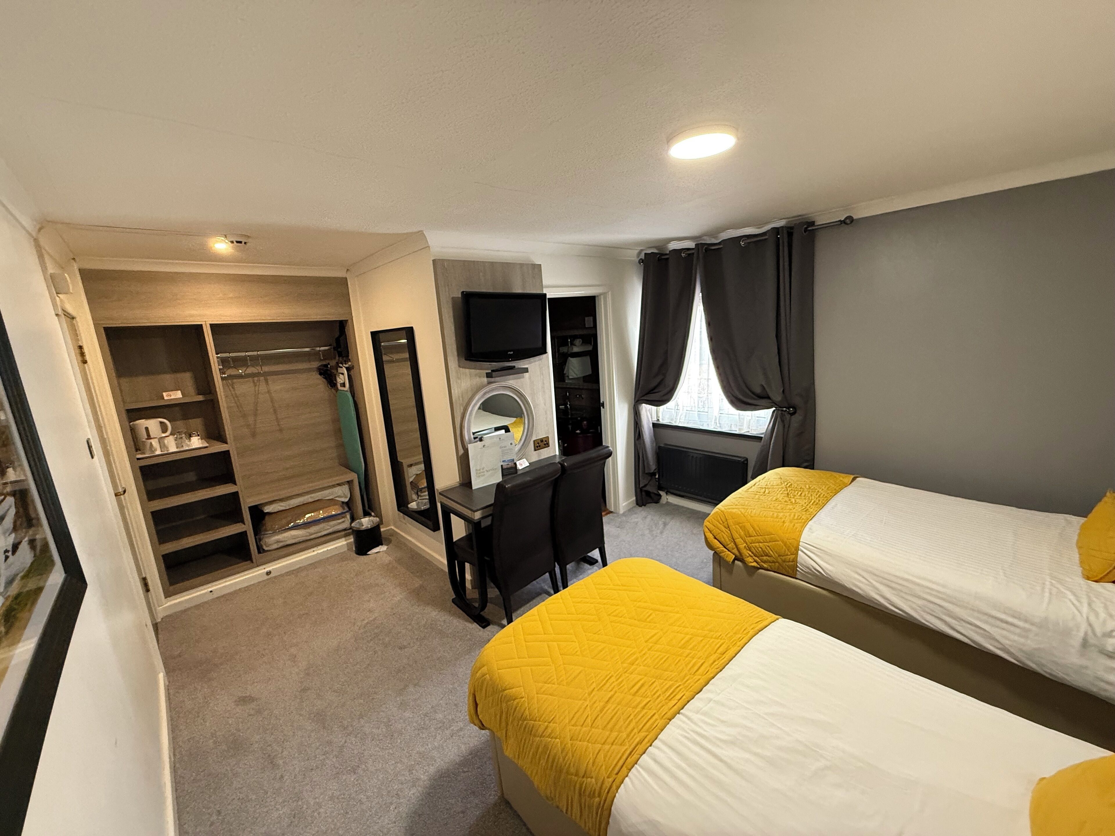 Ein Hotelzimmer mit zwei Betten, einem Schreibtisch, einem Fernseher und einem begehbaren Kleiderschrank.