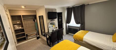 A hotel room with two beds, a desk, a TV, and a walk-in closet.