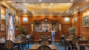 A bar area with wooden paneling, a counter, and a clock. There are tables and chairs arranged for dining. - Durrant House Hotel  (Bideford)