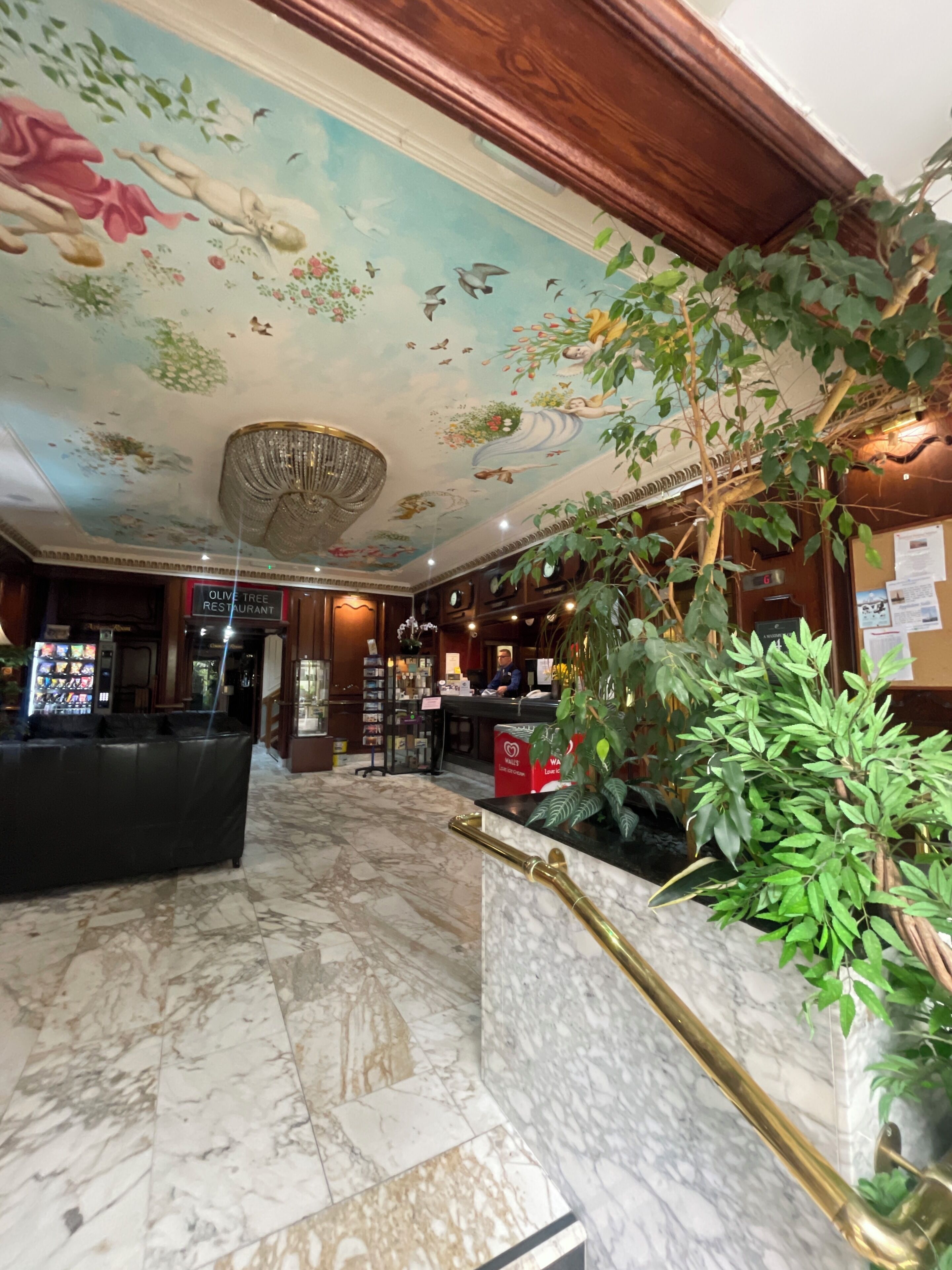 A lobby with a marble floor, a reception desk, a chandelier, and a mural on the ceiling.