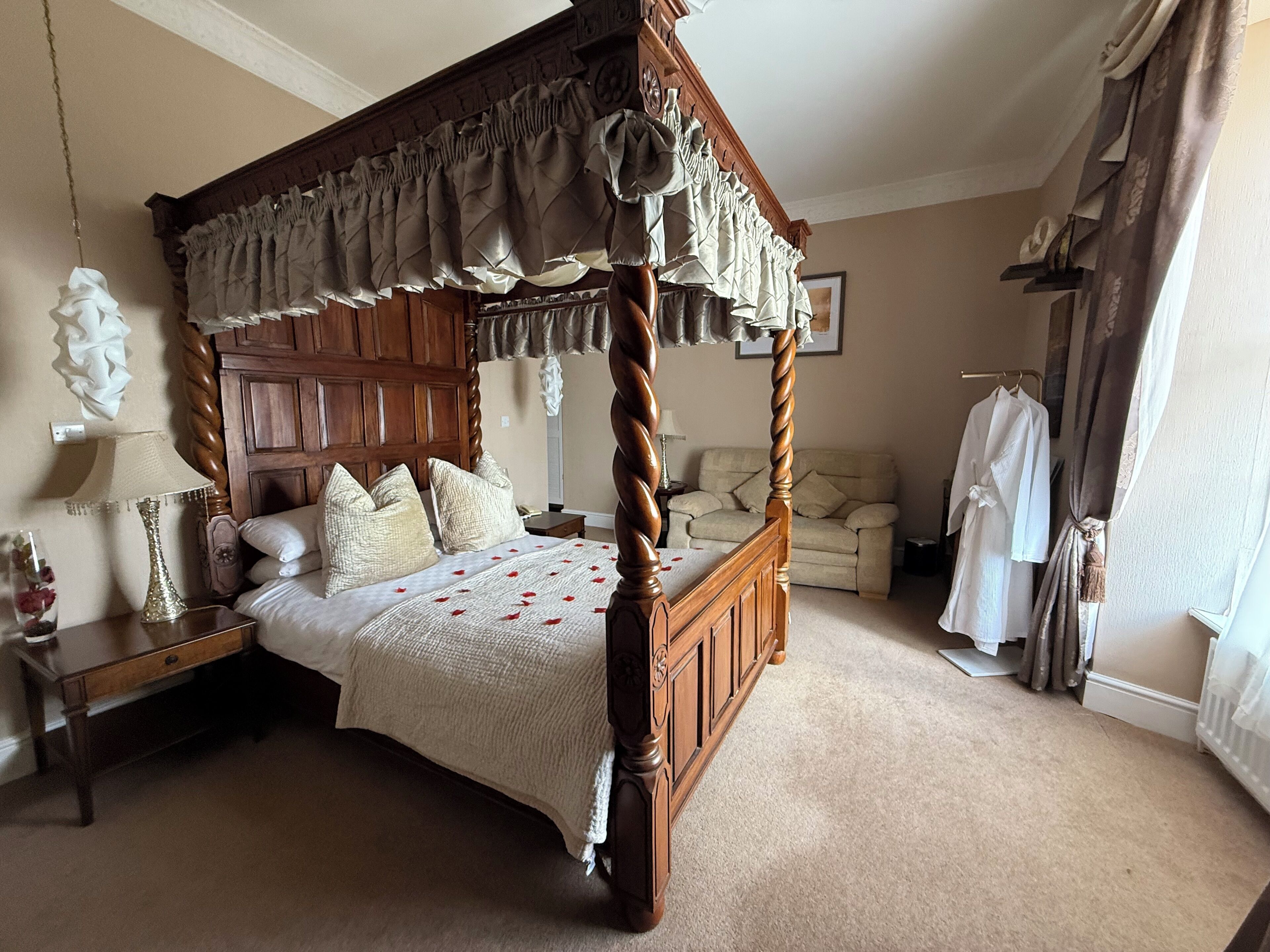 A four-poster bed with a wooden frame and a canopy, a bedside table with a lamp, a chair, and a radiator.