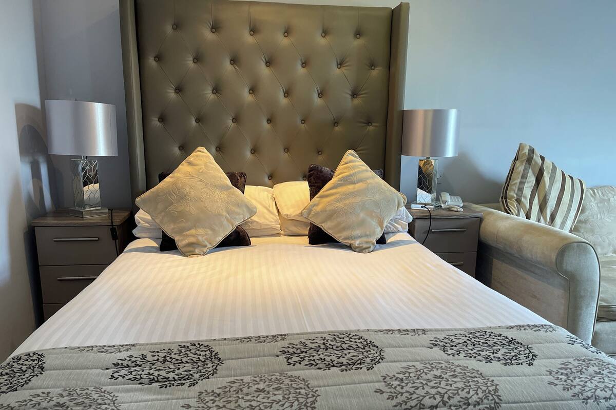 A neatly made bed with a tufted headboard, two bedside tables with lamps, and a sofa with striped cushions.