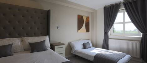 A bedroom with two beds, a nightstand, a window with curtains, and a wall-mounted artwork.
