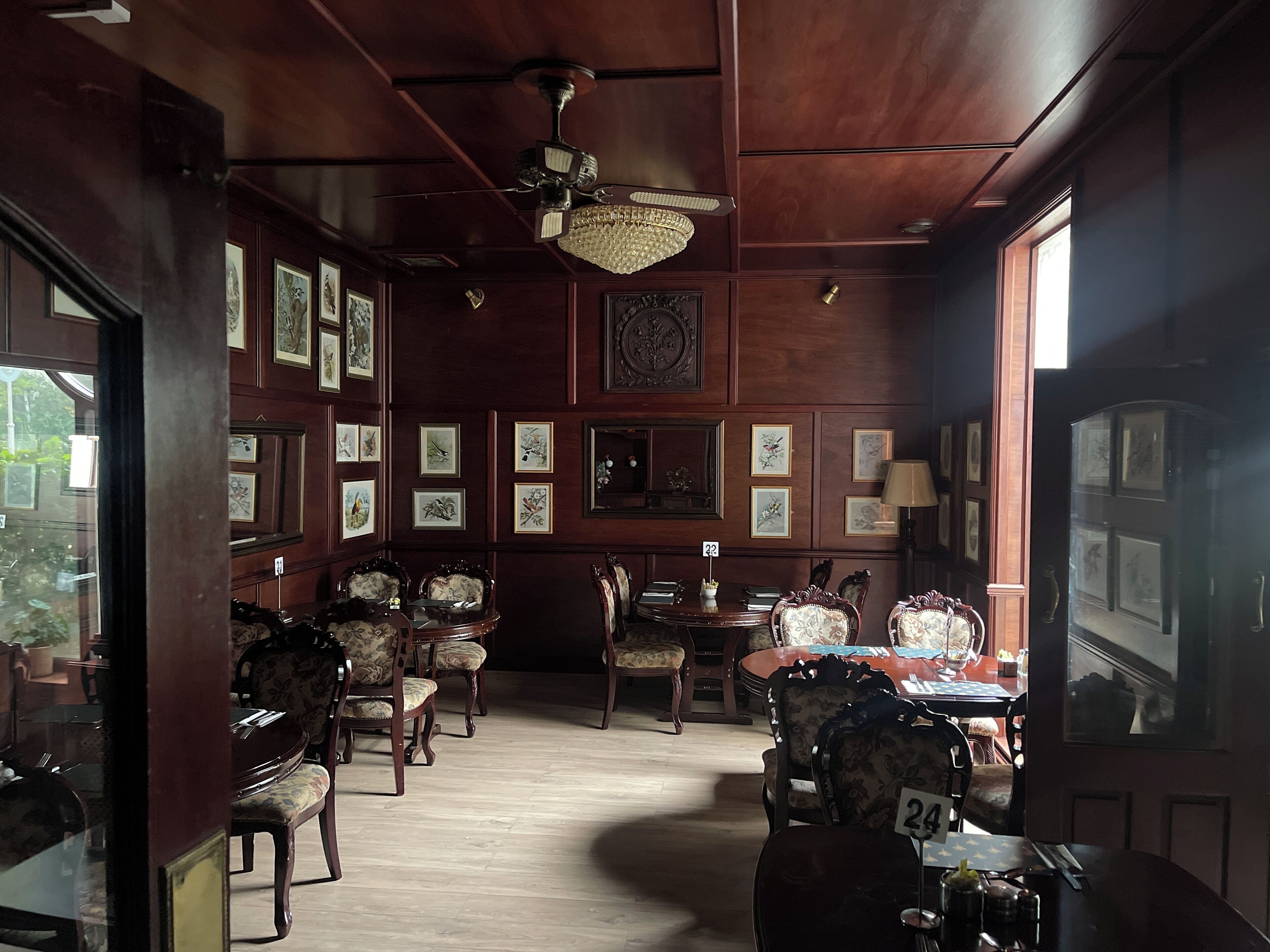A room with wooden paneling, framed artwork on the walls, a chandelier, and a dining area with numbered tables.