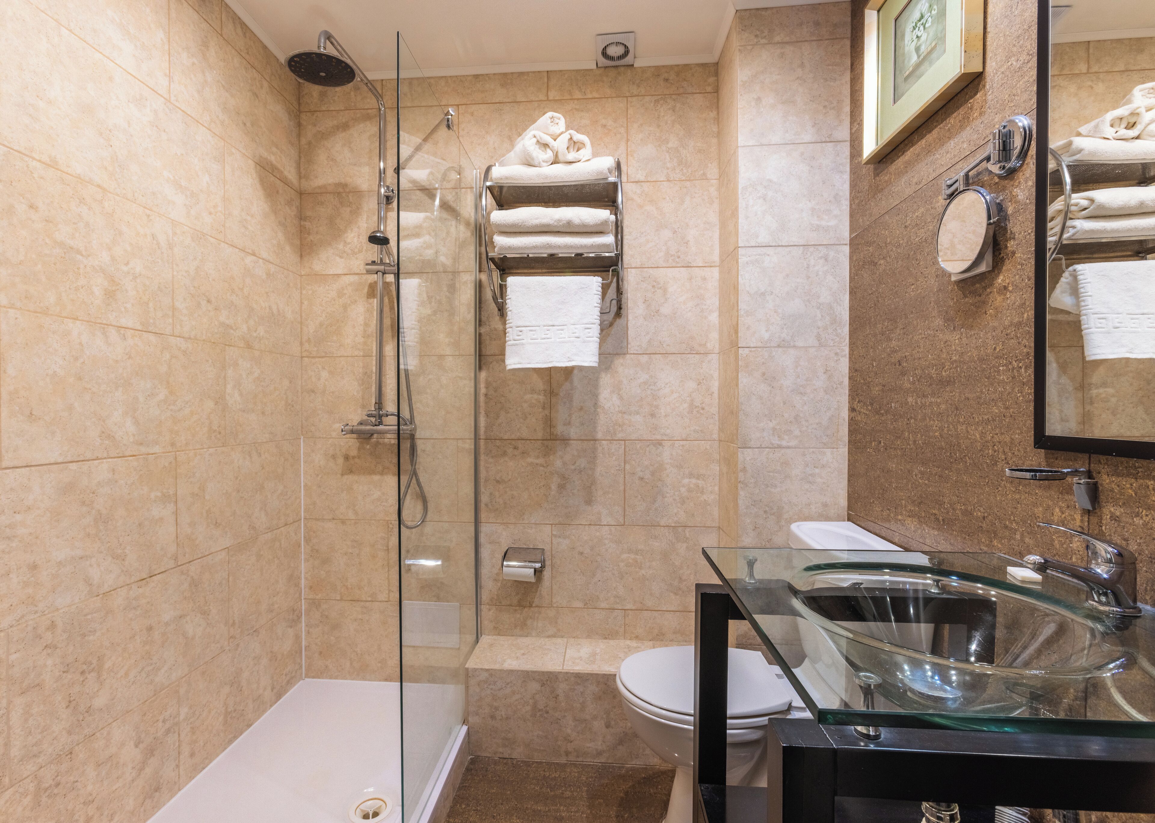Un bany modern amb plat de dutxa de vidre, un lavabo de vidre i un vàter.