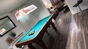 Une table de billard dans une pièce dotée d’un plancher en bois, d’un canapé et d’un coin bar.