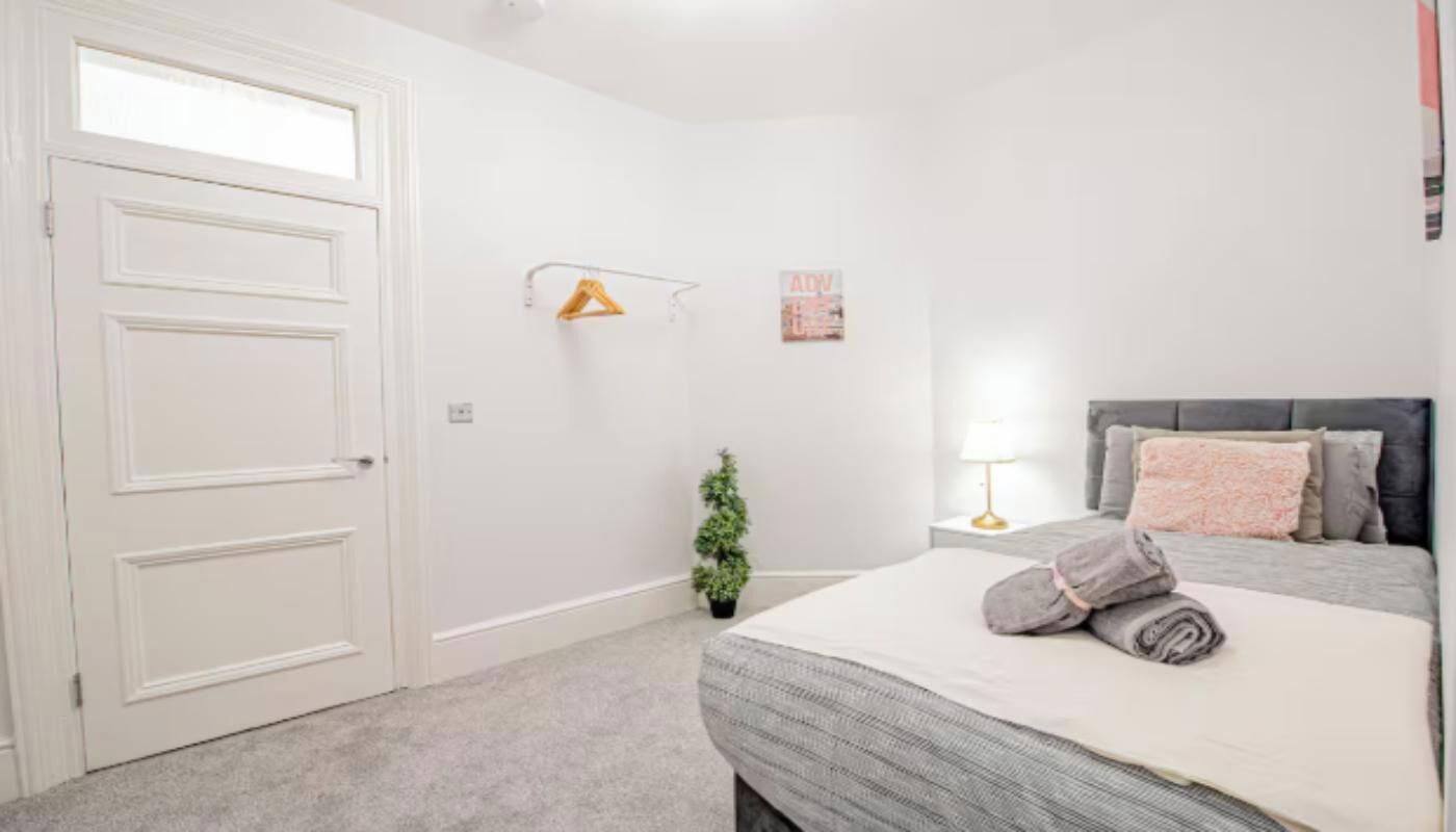 Une chambre à coucher avec un lit, une table de chevet, une lampe, une petite plante et une porte.