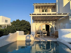 A pool area with a table and chairs, a covered seating area, and a clear view of the pool.