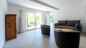 Ein geräumiges Wohnzimmer mit einem dunkelgrauen Sofa, einem Holzkasten und einem schwarzen Sessel.