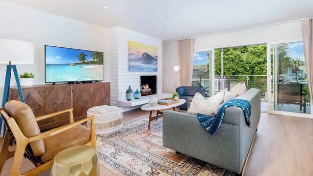 A modern living room with a fireplace, a large TV, and a balcony with a view of greenery.