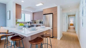 A modern kitchen with a central island, bar stools, and a stainless steel refrigerator.