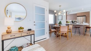 A modern kitchen with a dining area, a round mirror, and a wooden console table.