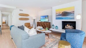 A modern living room with a sofa, armchairs, a coffee table, a TV, and a fireplace.
