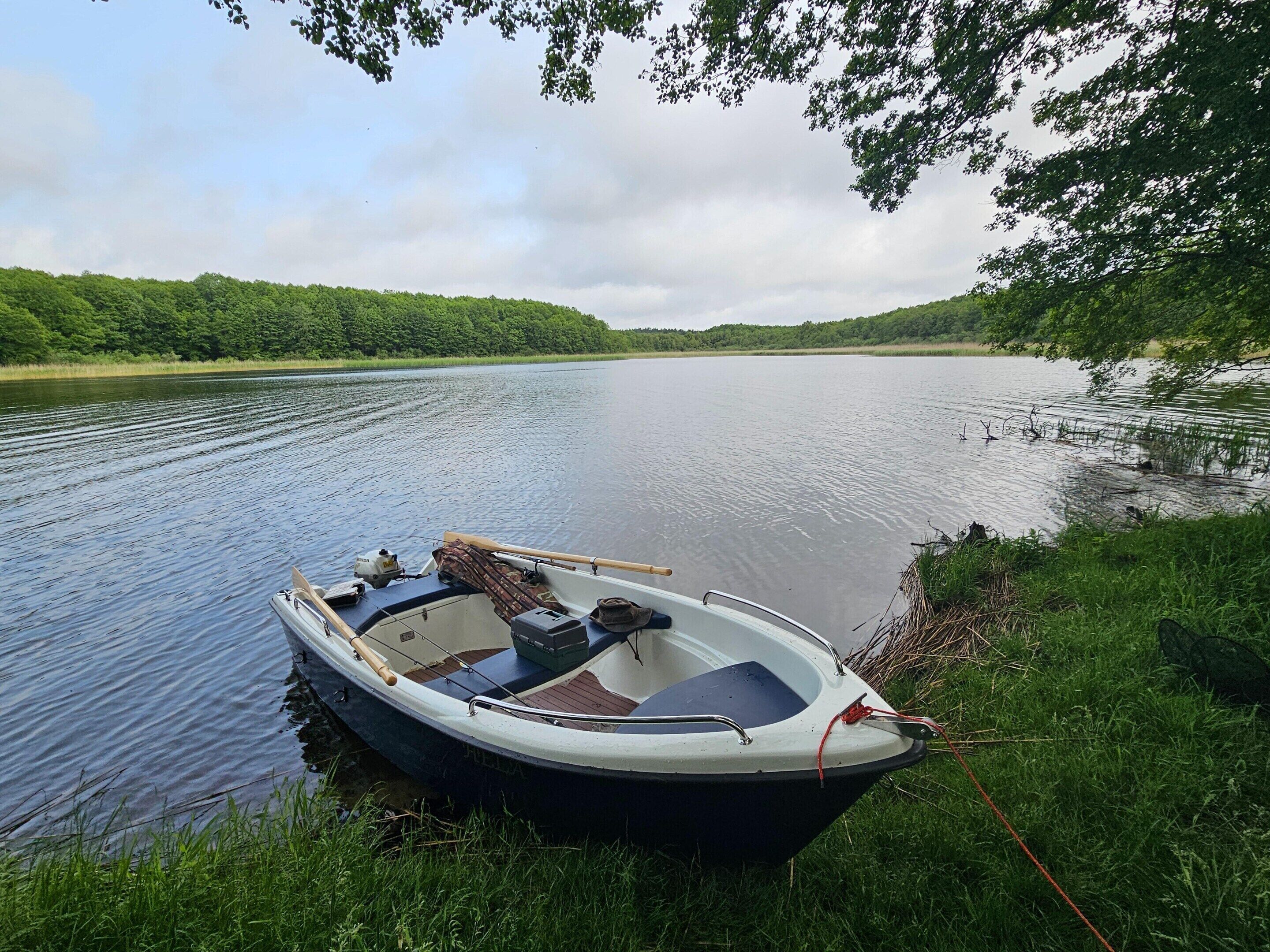 A small boat docked at the edge of a calm river, surrounded by lush greenery and trees.