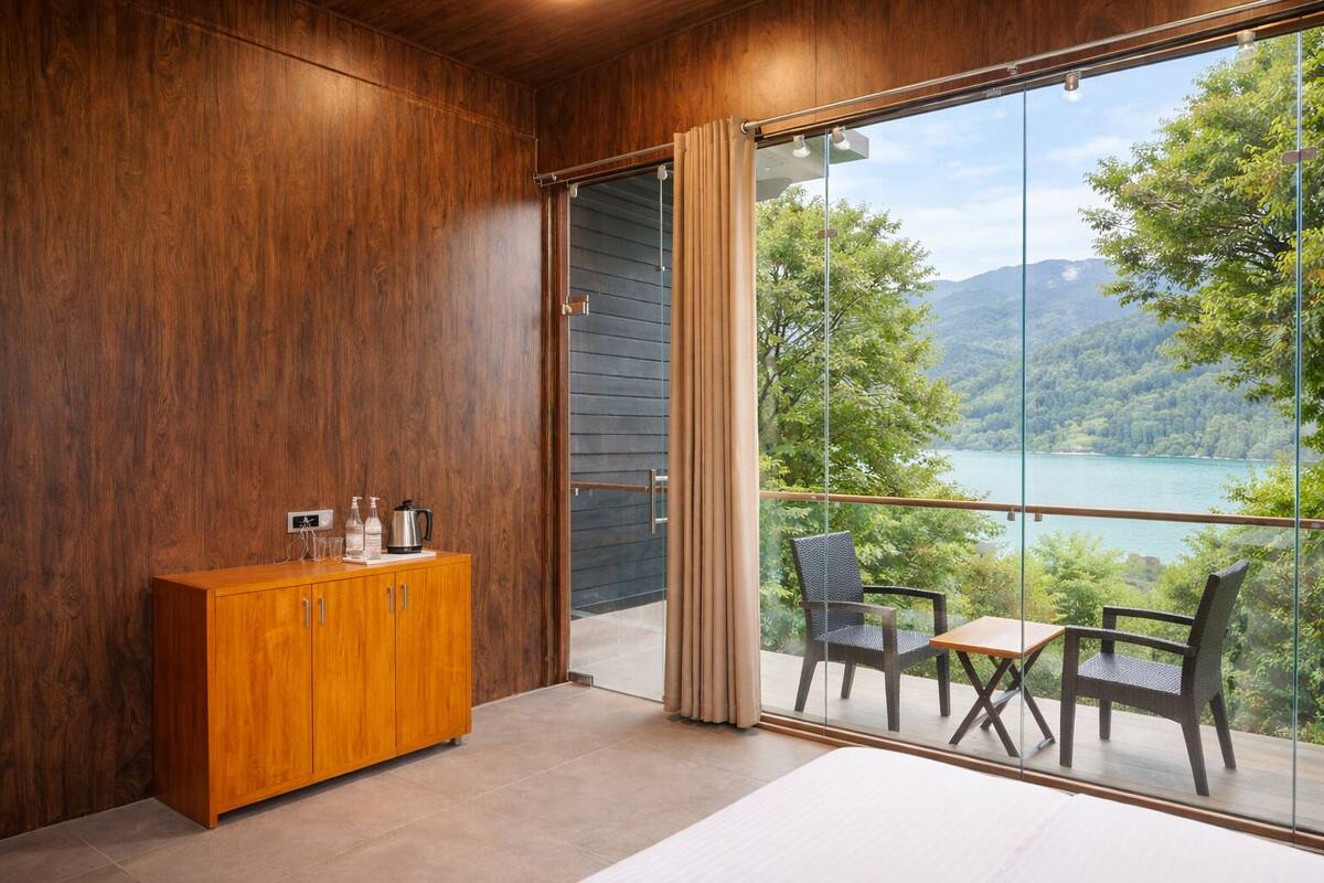 A room with a wooden cabinet, a bed, and a balcony with chairs and a table overlooking a lake.